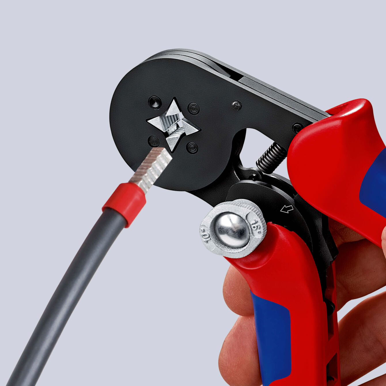 The image shows a cable cutter being held by a hand. It has red grip areas and a black working surface where a cable is being handled.