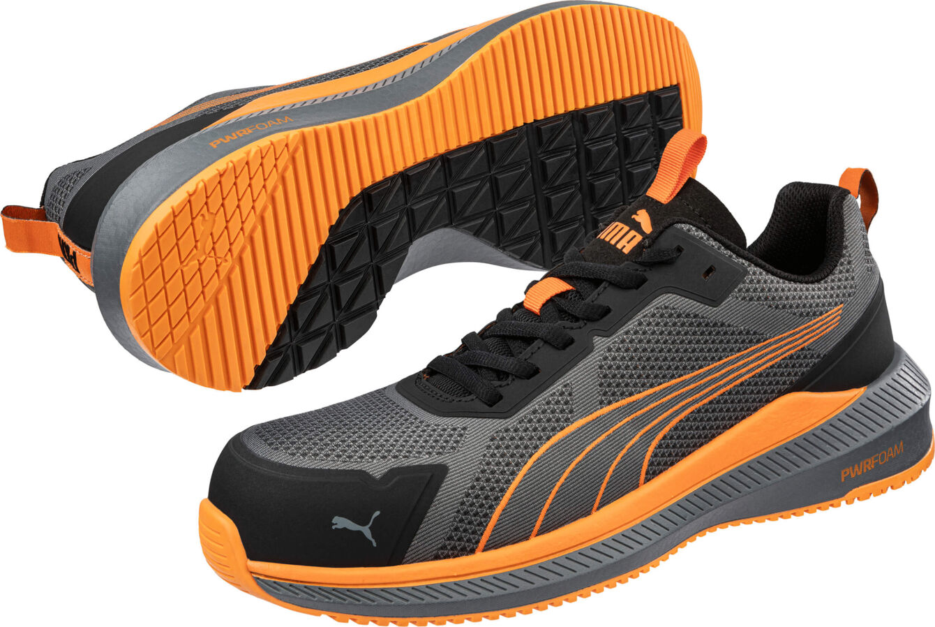 The image shows athletic shoes in black and gray with orange accents. The sole has a textured surface, and a logo is prominently placed on the side.