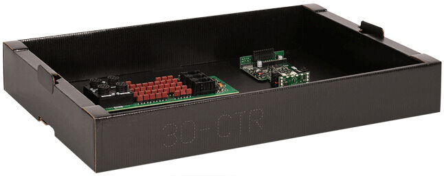 The image shows a black, flat box with two circuit boards on it. One board has red and black connectors, while the other is smaller and has various components. The box is labeled.