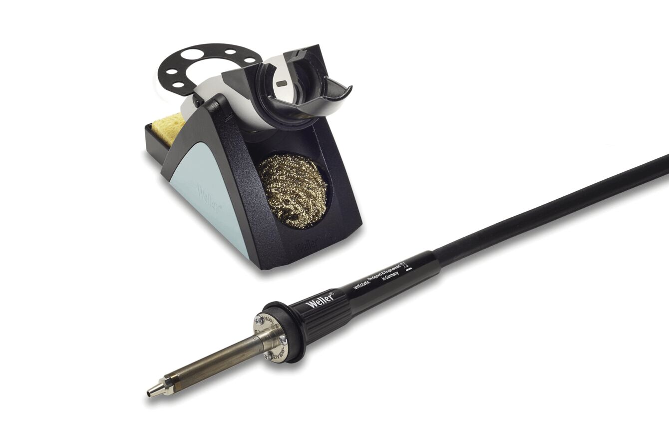 The image shows a soldering iron with a black cable and a soldering station. The station has a gray and black color scheme, a sponge, and a metal brush for cleaning the soldering iron.