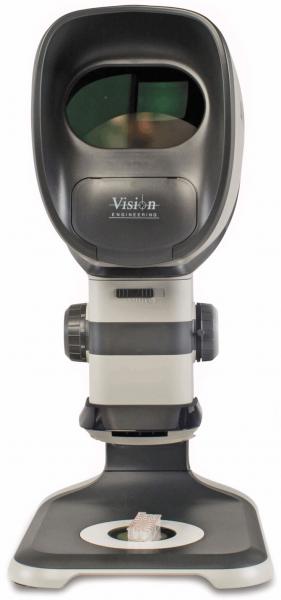 The image shows a medical device for eye examinations. It has an oval, black frame with a lens at the front, and a sturdy, gray base.