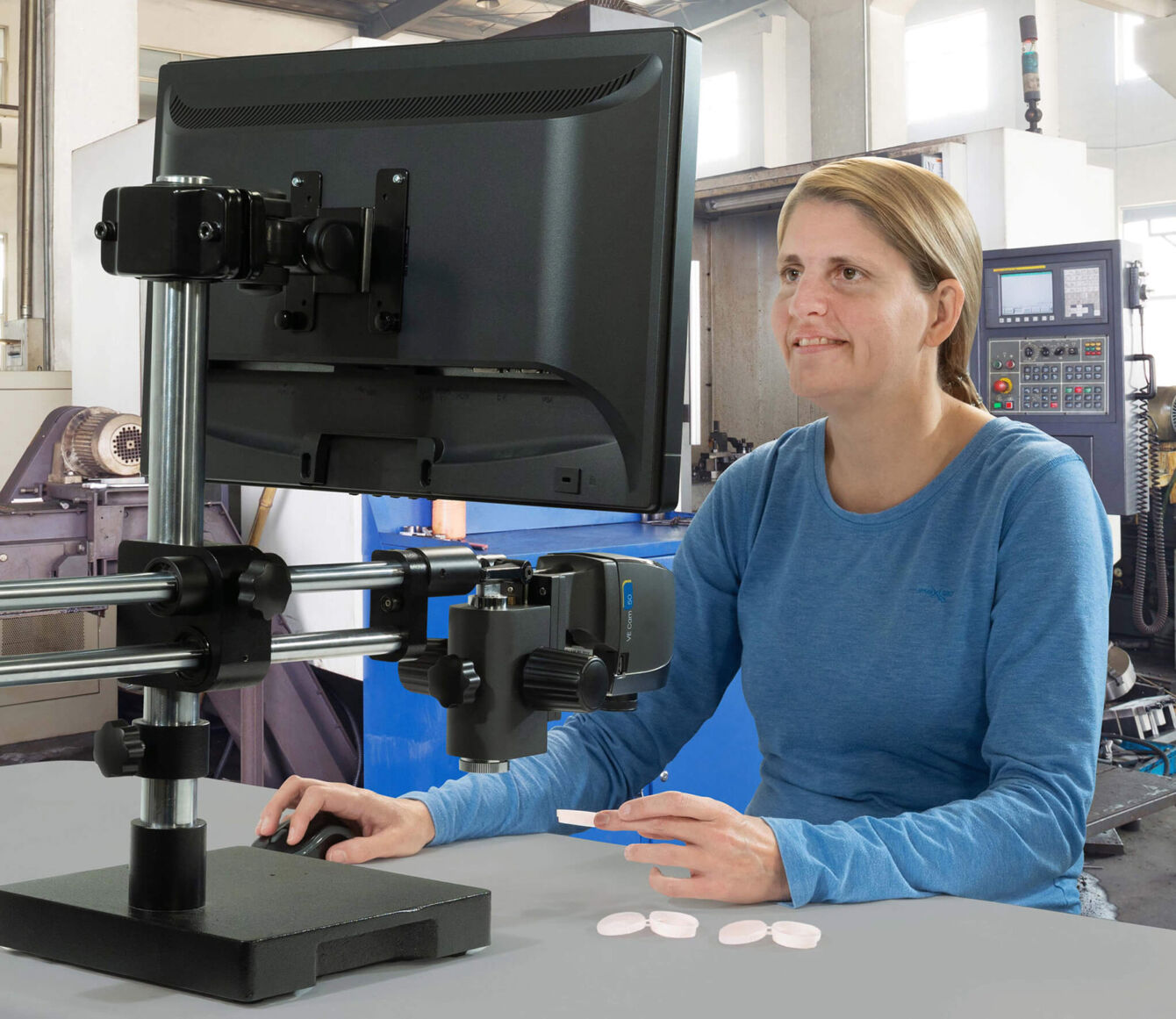 A person is sitting at a table in front of a monitor mounted on a movable stand. They are wearing a long-sleeved, blue shirt and holding small round objects in one hand.