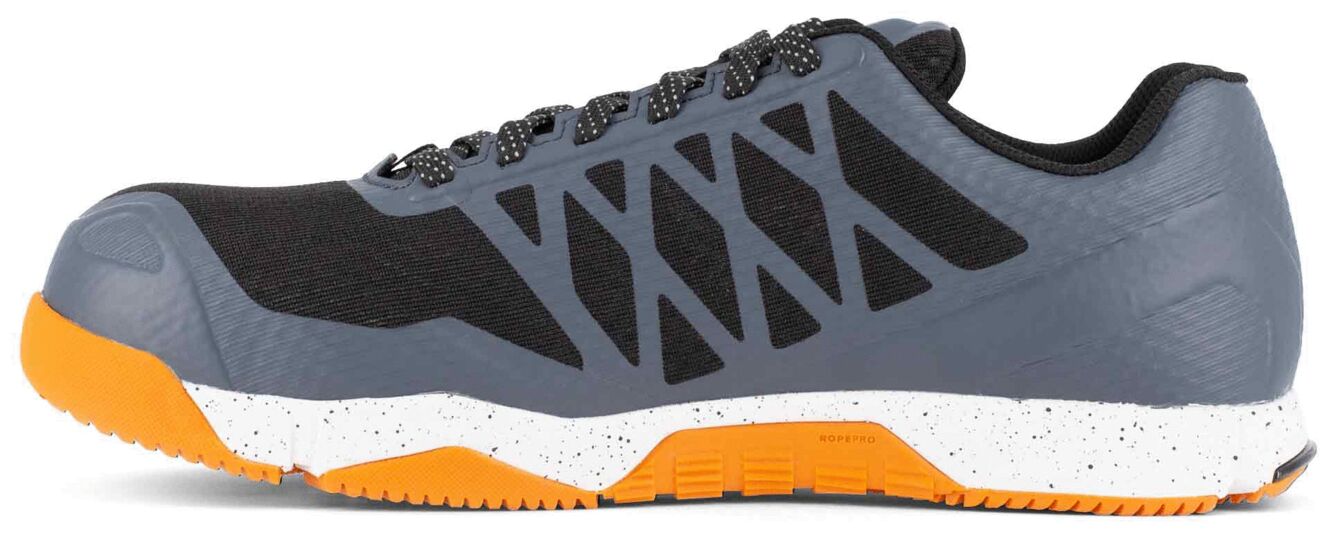 The shoe is sporty, featuring a gray and black color scheme with an orange sole area. The sole is flat and textured, ideal for high-movement activities.