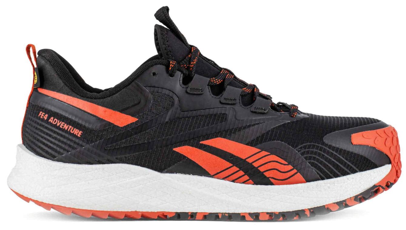 The shoe is sporty and sturdy, predominantly black with orange accents. It has a textured surface, a high, white sole base, and a non-slip rubber sole.