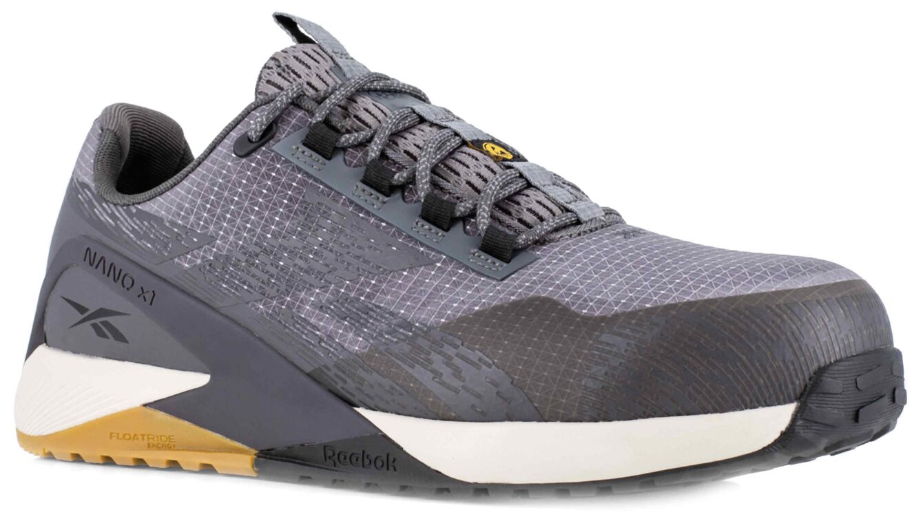 The shoe is a gray fitness shoe with a textured surface, flat sole, and sturdy, lightweight material. The laces are dark gray, and the sole has white and gold accents.