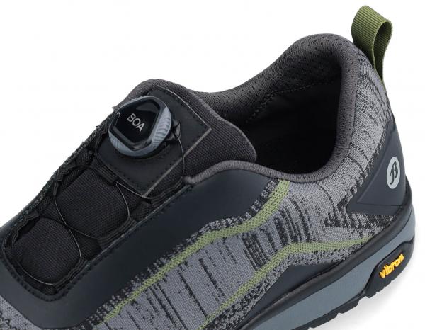 The image shows a modern, gray shoe with a textured upper. It features a Boa closure system and a profiled sole for good grip. A green line runs along the side.