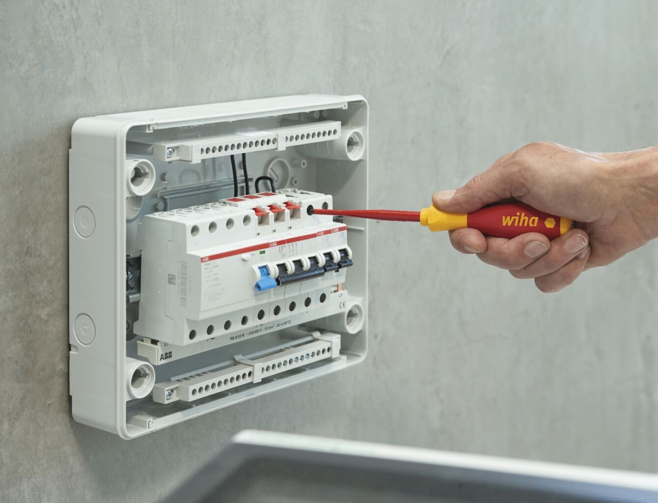 A craftsman is working on an electrical distribution box on a wall. He is holding a red screwdriver and is screwing on components in the box, which appears illuminated and modern.