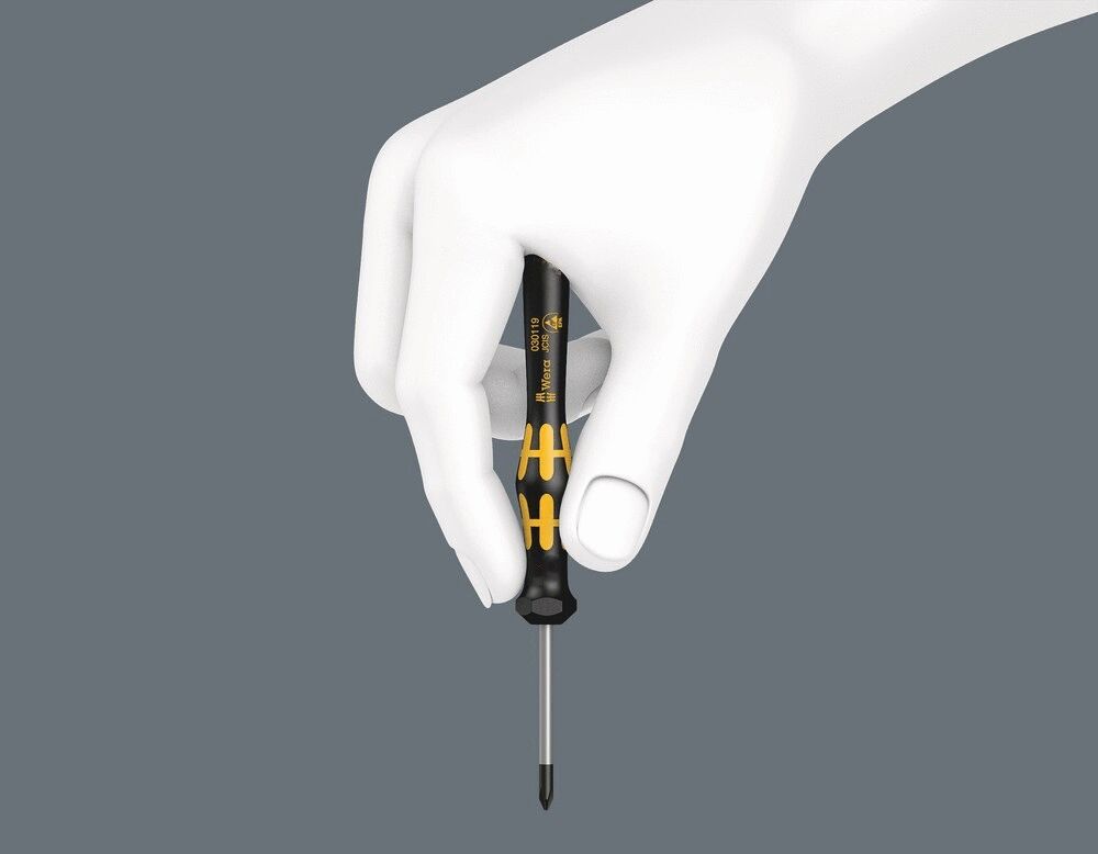 The image shows a hand holding a screwdriver with a black handle and yellow accents. The screwdriver has a pointed blade and is held vertically. The background is gray.