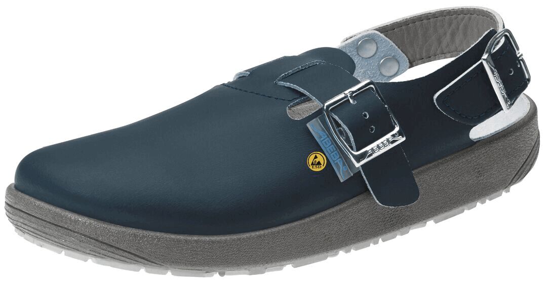 The shoe is a black clog made of smooth material. It has a wide, closed front area, an adjustable strap with a buckle, and a non-slip, gray sole.